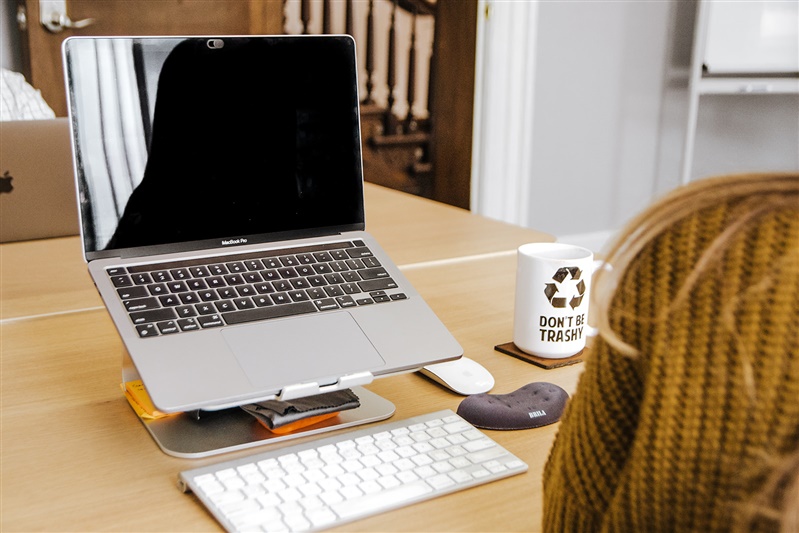 Apple laptop on laptop stand with monitor and mouse and "don't be trashy" mug